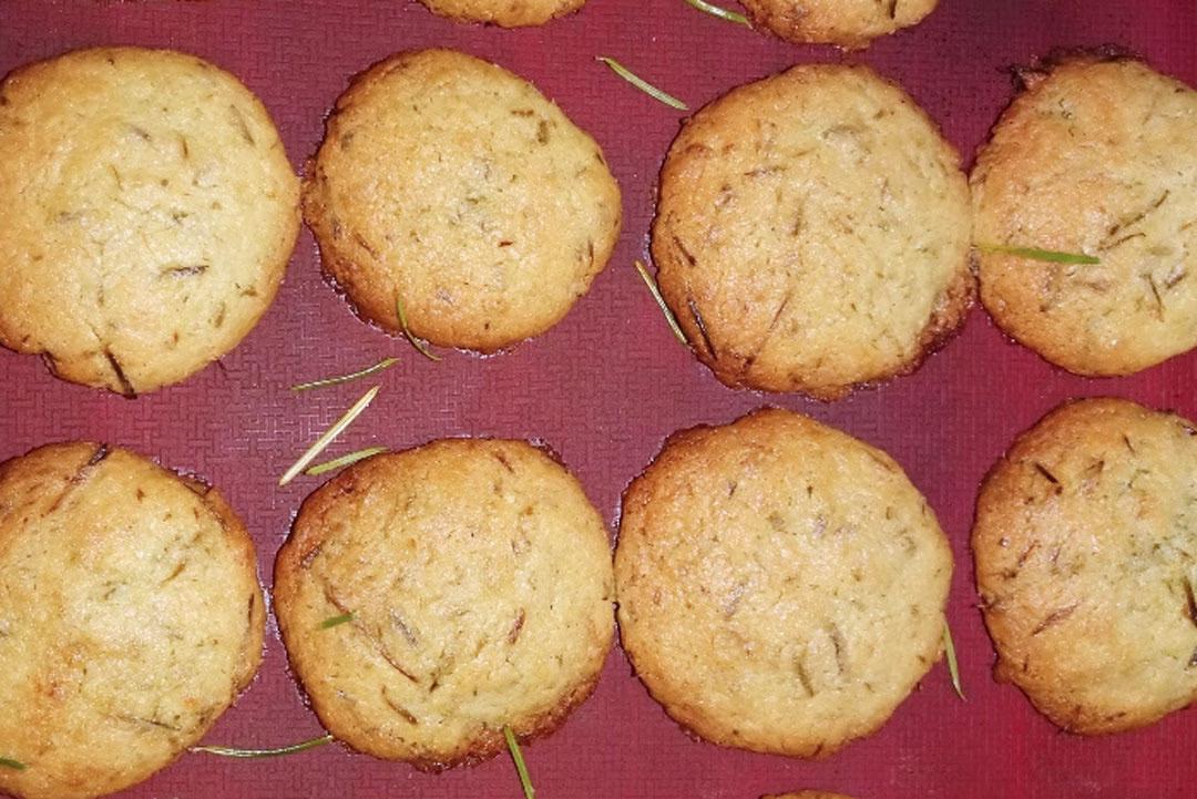 Nadelbaumküche: Mehrere goldbraune, runde Kekse mit Fichtennadeln liegen auf einer roten Backmatte.