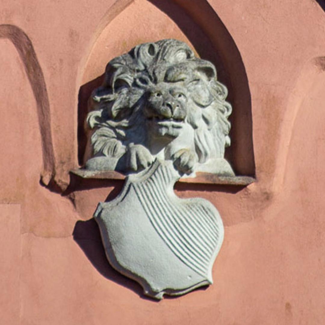 Steinlöwe mit Schild an einer rosafarbenen Fassade – eines der verborgenen Details im Lübecker Domviertel.