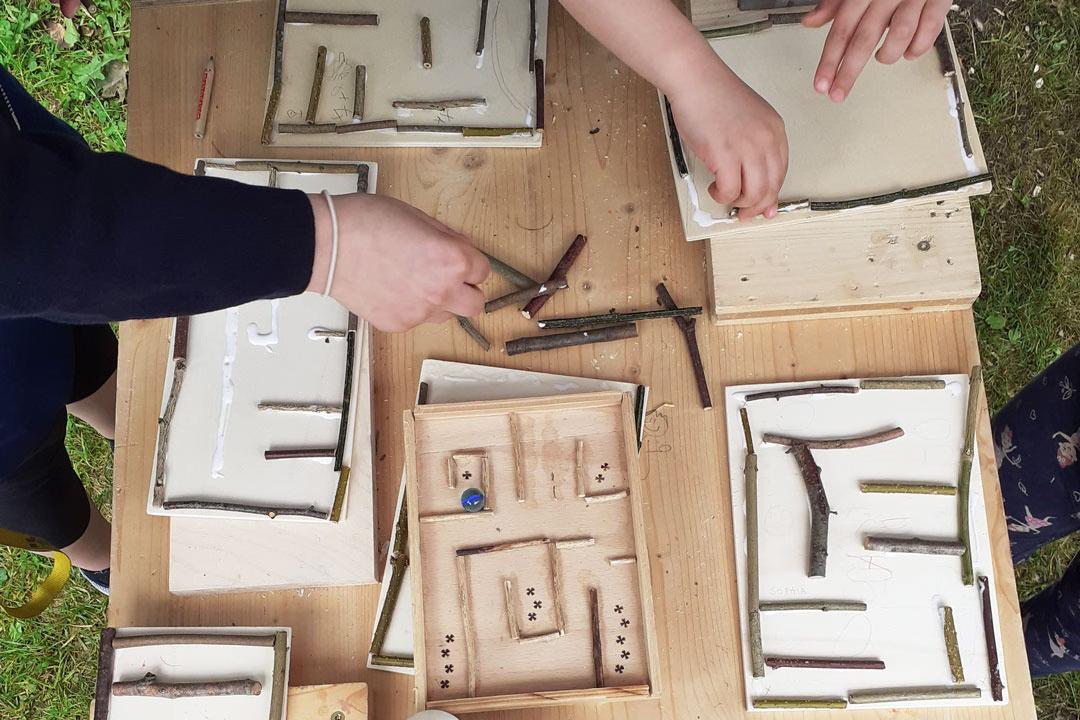 Familien-Holzwerkstatt: Kinder gestalten kreative Holzlabyrinthe mit Zweigen und bauen eigene Spiele in der Werkstatt.