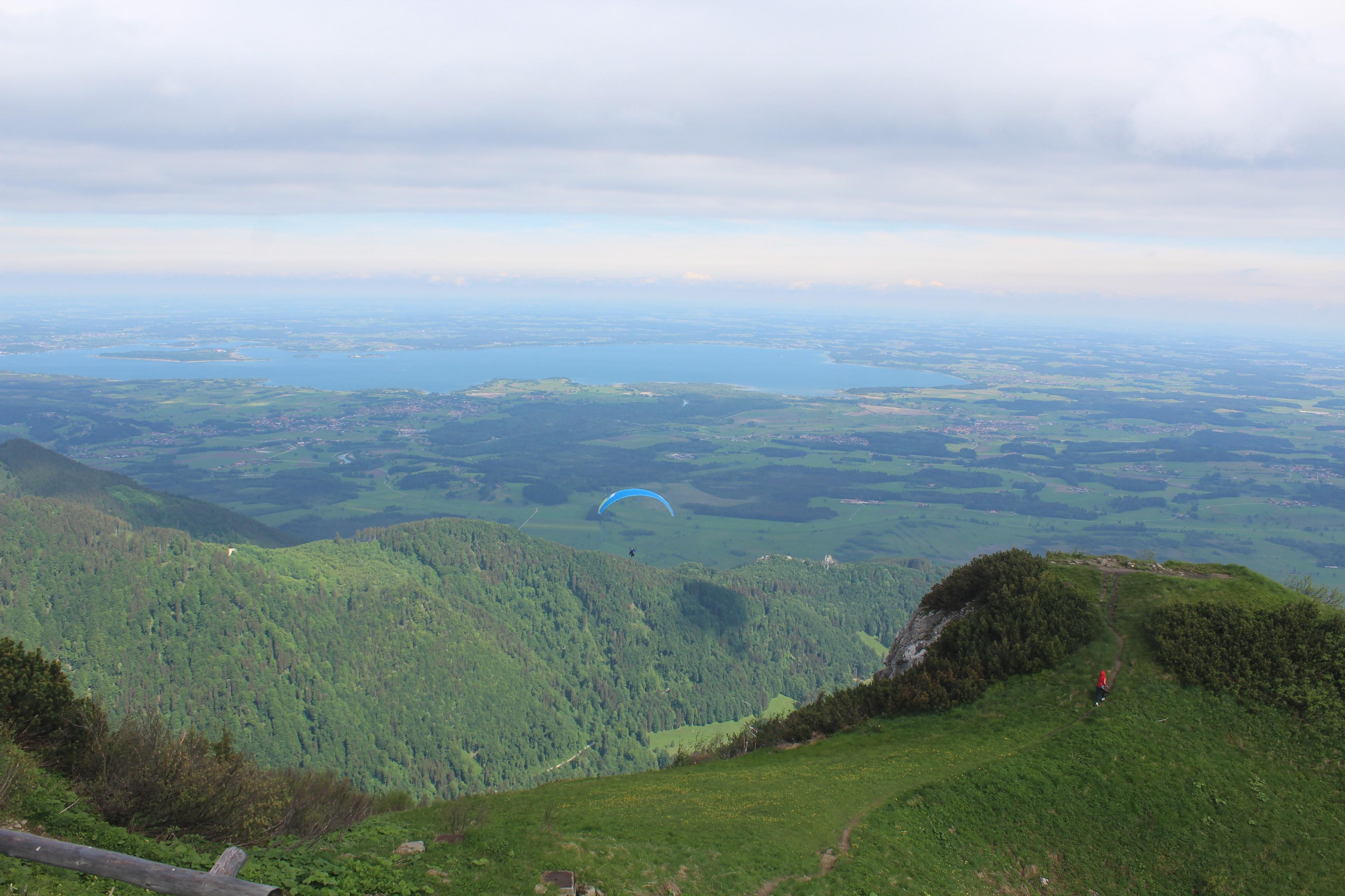 Ein Gleitschirm über bewaldeten Berghängen mit dem Chiemsee im Hintergrund