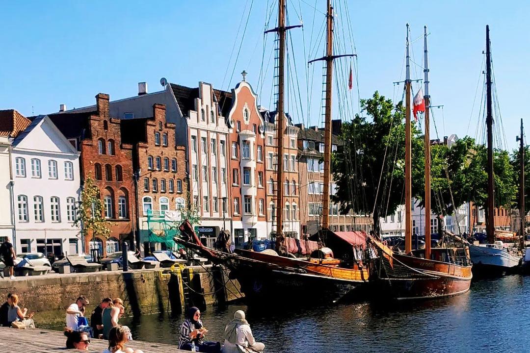 Möglicher Stopp der Radtour: Historische Lübecker Häuser am Hafen mit segelnden Traditionsschiffen und Menschen am Ufer.