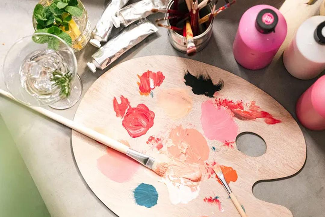 Pinsel, Farben und eine Mischschale aus Holz auf einem Tisch bei der ArtNight.