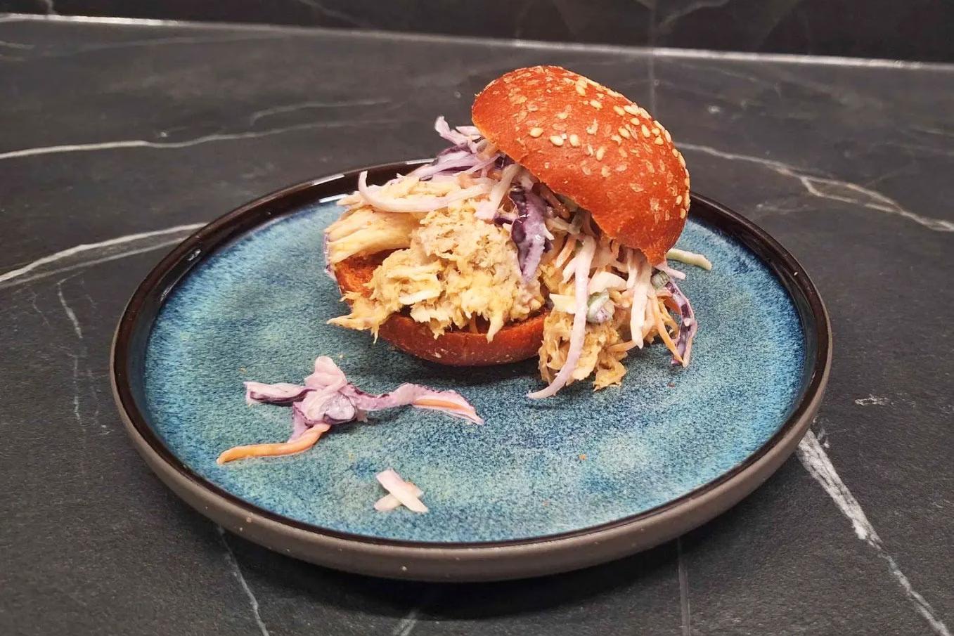 Das Ergebnis des Afterwork Burger-Grillkurs: Ein Mini-Burger auf blauem Teller, mit goldigem Brioche, Salat und Fleisch.