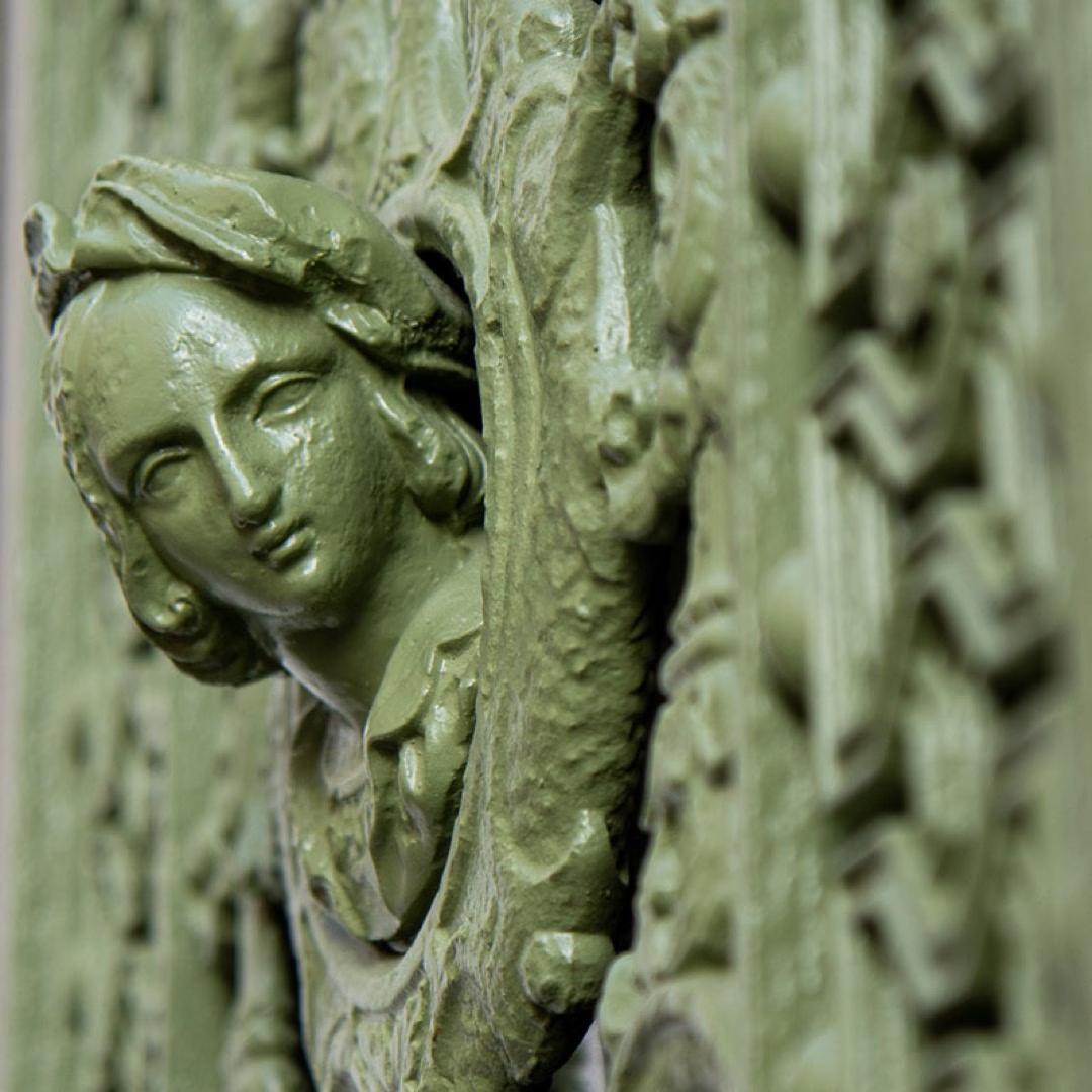Detail einer grün gestrichenen Tür mit filigranem Relief und dem Gesicht einer Frau in Lübeck.