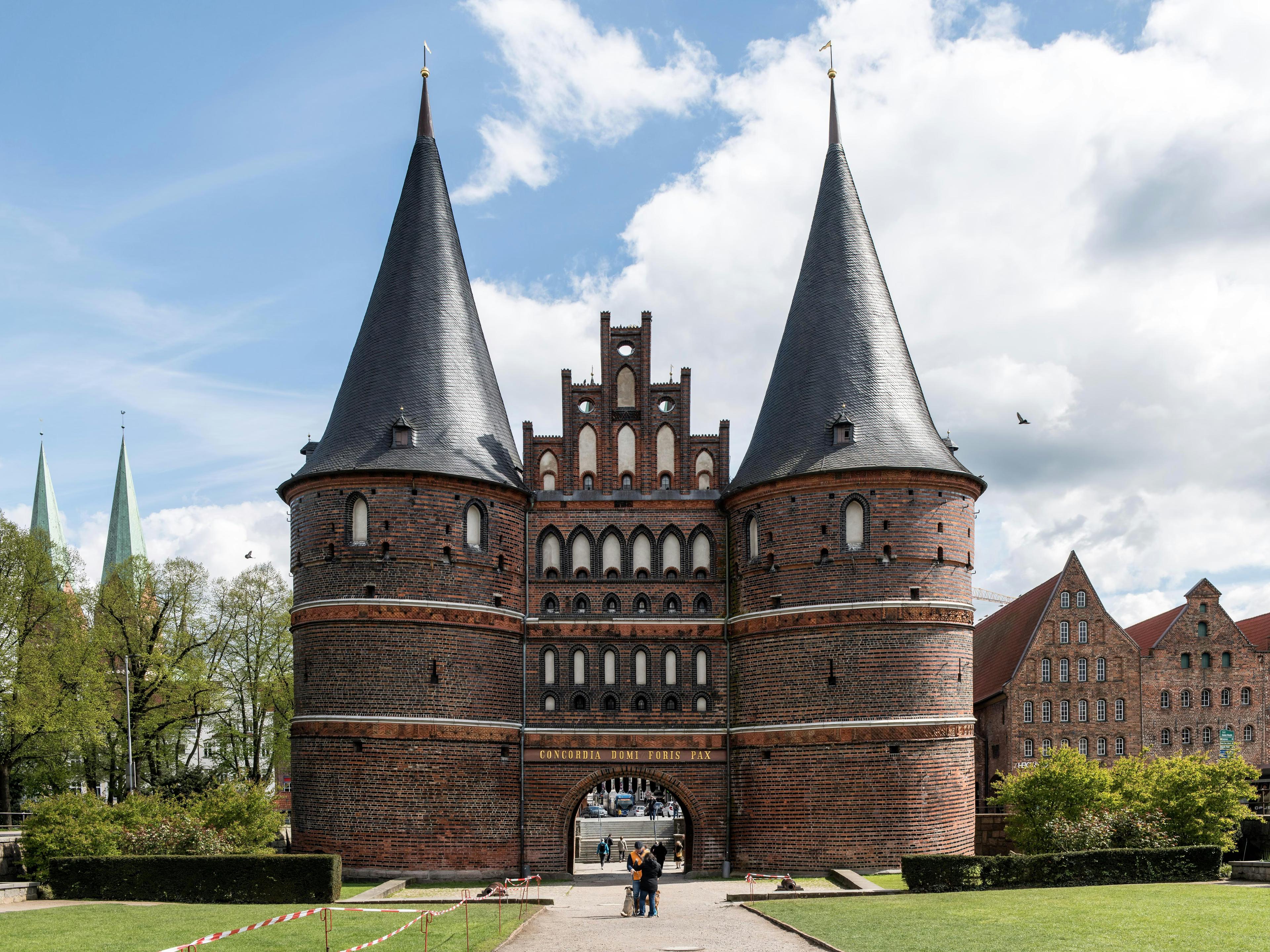 Das Holstentor in Lübeck mit zwei Türmen vor blauem Himmel, davor eine grüne Wiese.