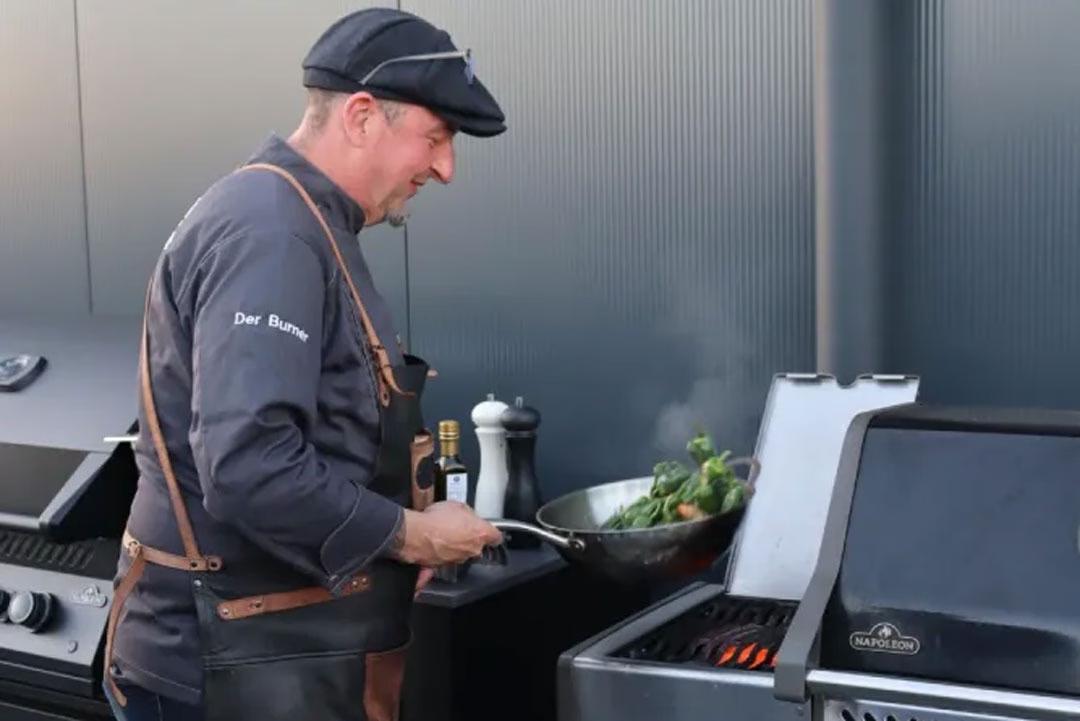 Profi-Grillmeister bereitet frisches Gemüse in der Pfanne am Gasgrill zu.