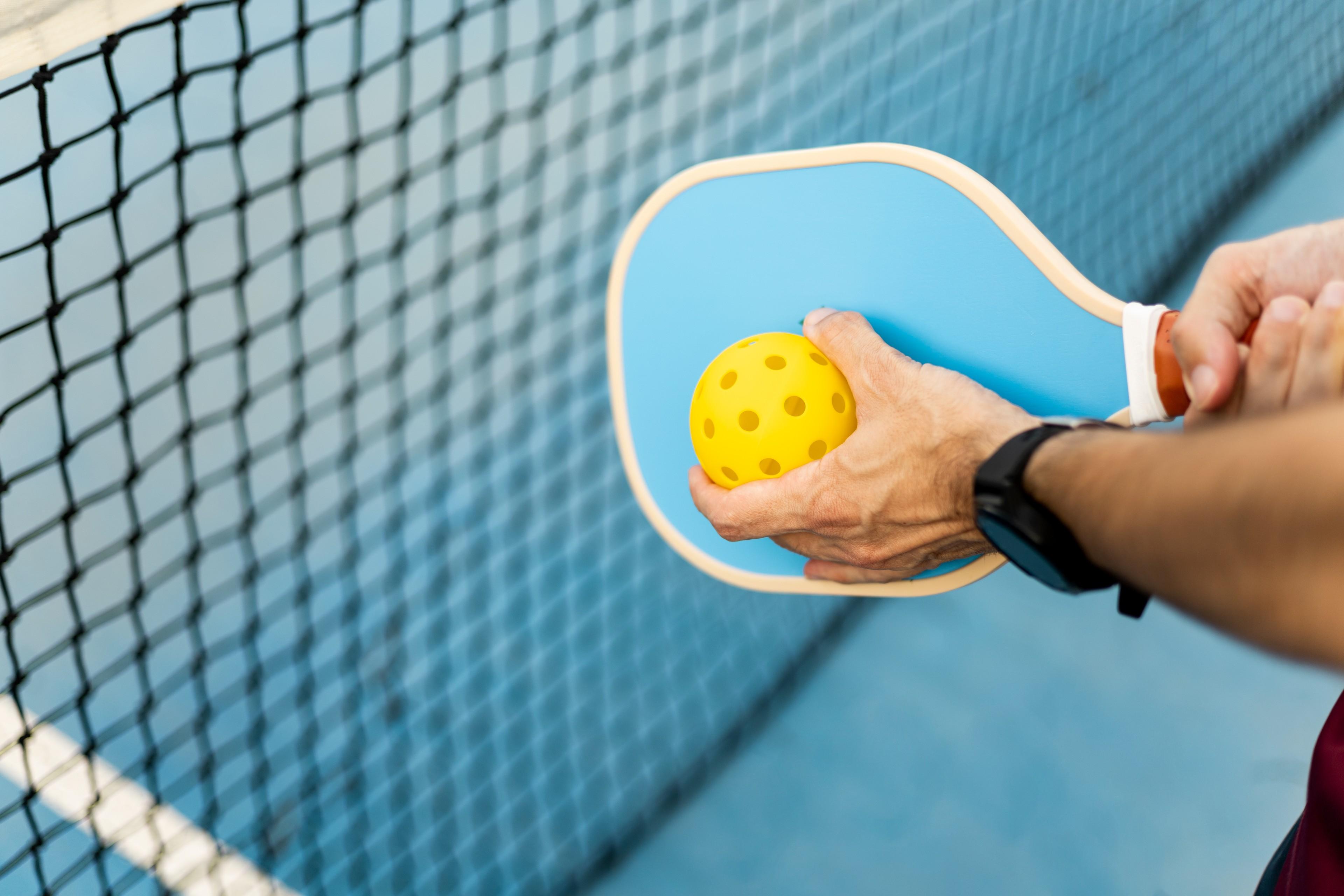 Schläger und Hand, die einen Pickleball hält