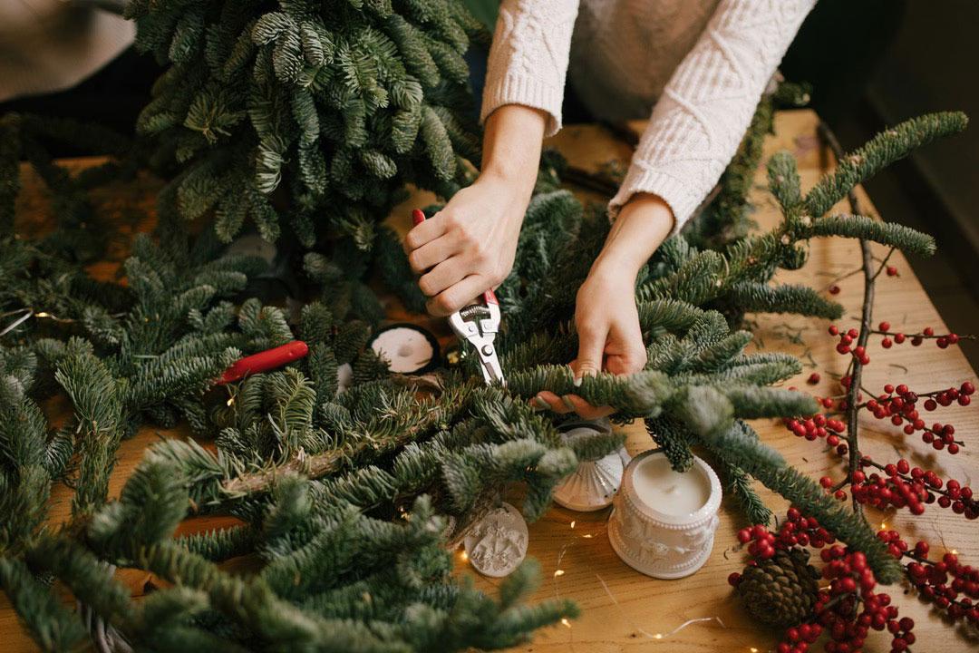 Eine Person schneidet auf einem Tisch Zweige im DIY-Workshop: Adventskranz binden in Lübeck.