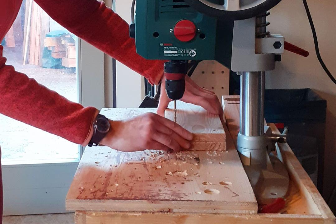Teilnehmerin beim Mädelsabend in der Holzwerkstatt: Sie bohrt präzise Löcher in ein Holzbrett mit der Ständerbohrmaschine.