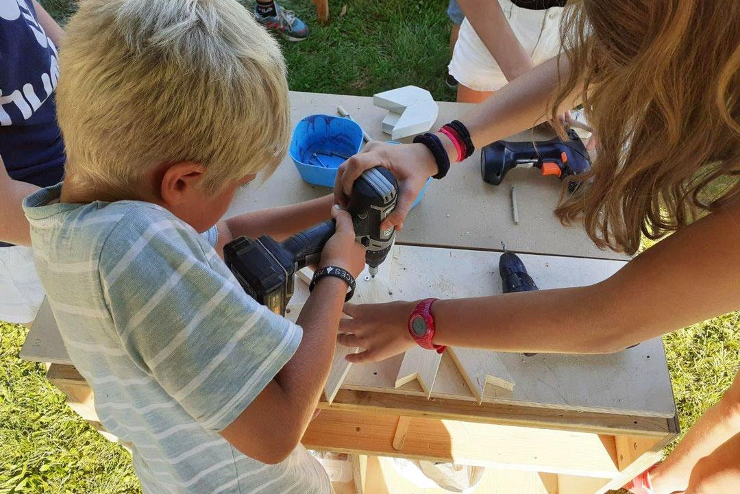 Familien-Holzwerkstatt: Ein Junge arbeitet mit Akkuschrauber und Holz und lernt handwerkliche Techniken spielerisch kennen.