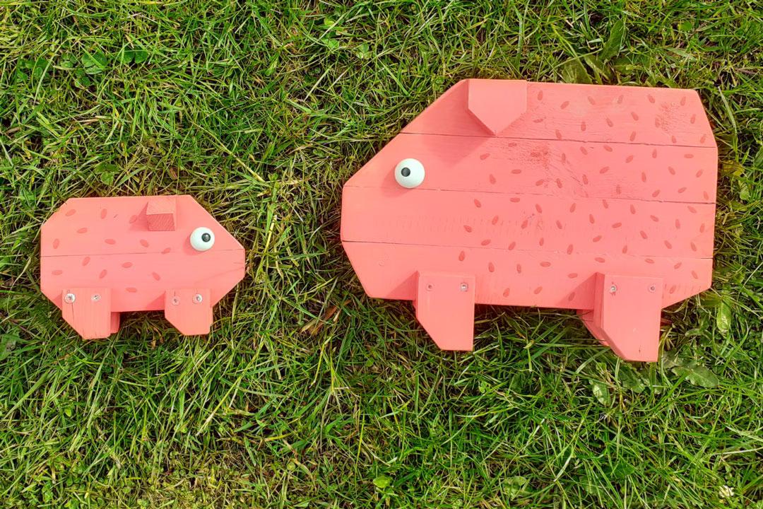 Familien-Holzwerkstatt: Zwei selbstgebaute Holzschweine liegen auf der Wiese, kreative Ergebnisse des Familienkurses.