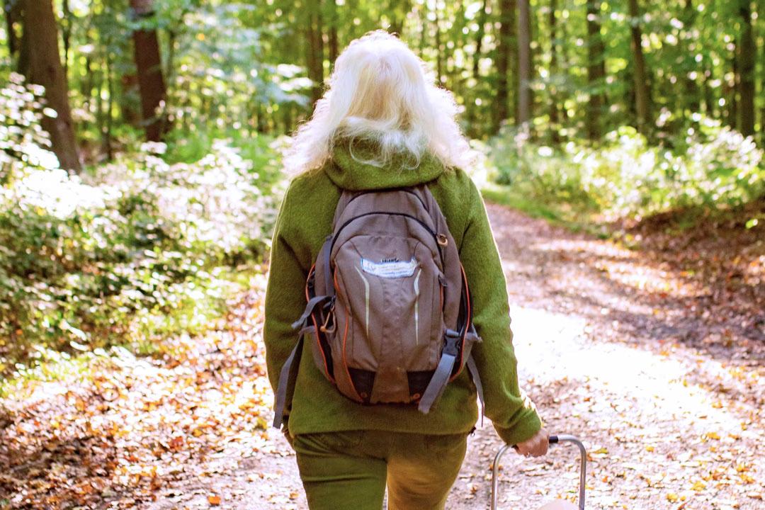 Die Naturführerin mit Rucksack läuft auf einem Waldweg bei einer Waldführung.