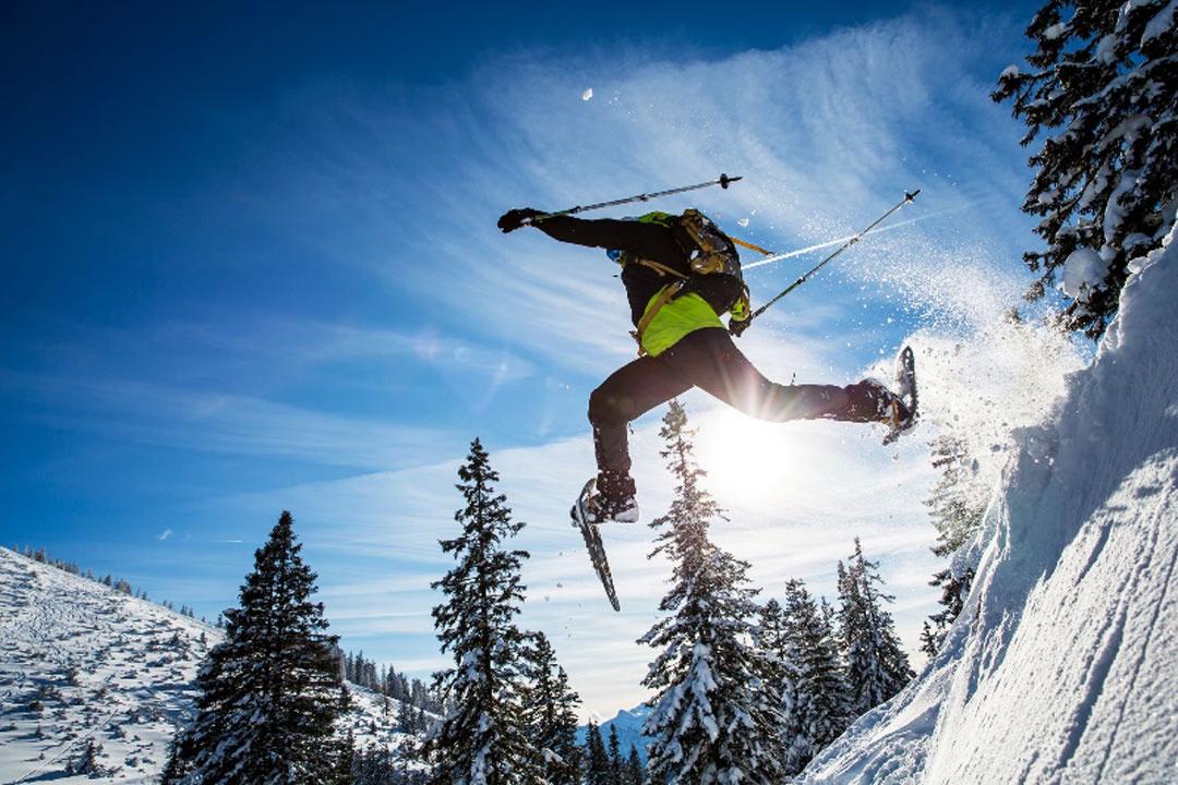 Action beim Schneeschuhwandern: Teilnehmer springt einen Berghang hinab.