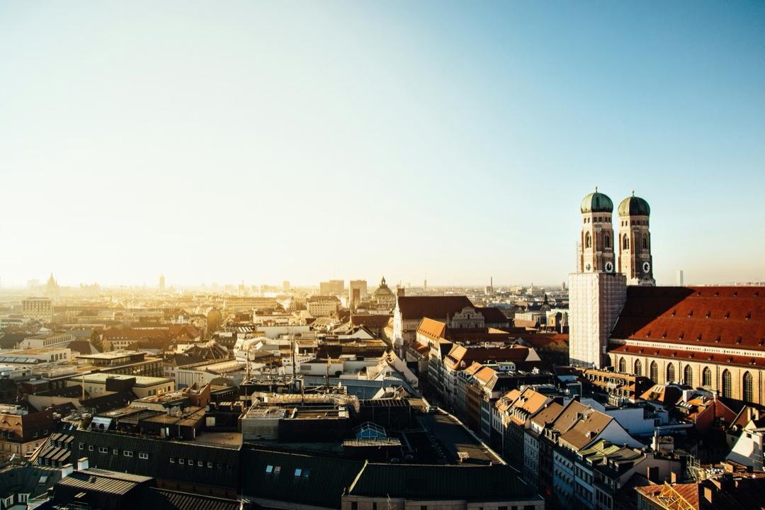 Stadtansicht von München im Sonnenschein, mit den Zwiebeltürmen der Frauenkirche, die über der Altstadt thronen.