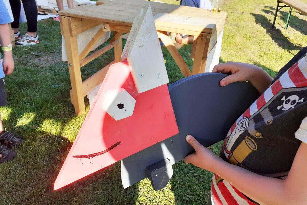 Familien-Holzwerkstatt: Kind präsentiert stolz eine selbstgebaute bunte Holzfigur, kreativ bemalt und zusammengesetzt.