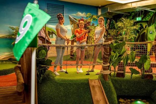 minigolf-fahne-im-vodergrund-drei-fraue-mit-minigolfschlägern