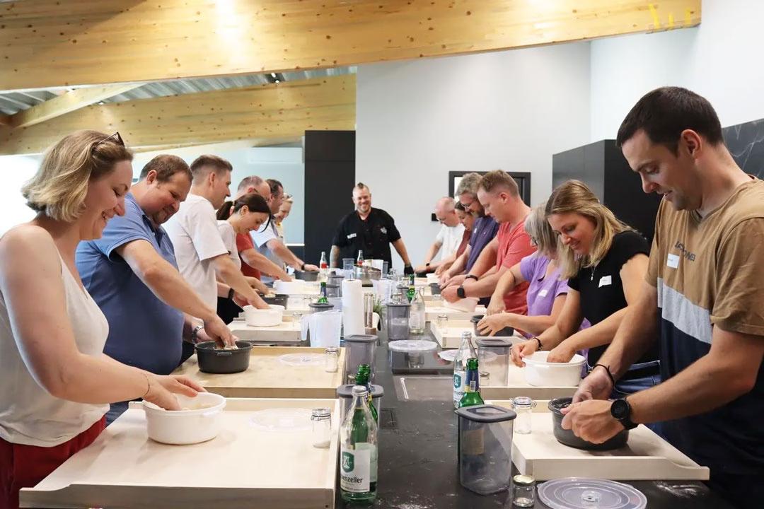 Pizza backen lernen in der Gruppe: Kursteilnehmer:innen kneten gemeinsam Pizzateig im Pizzabackkurs-Workshop.