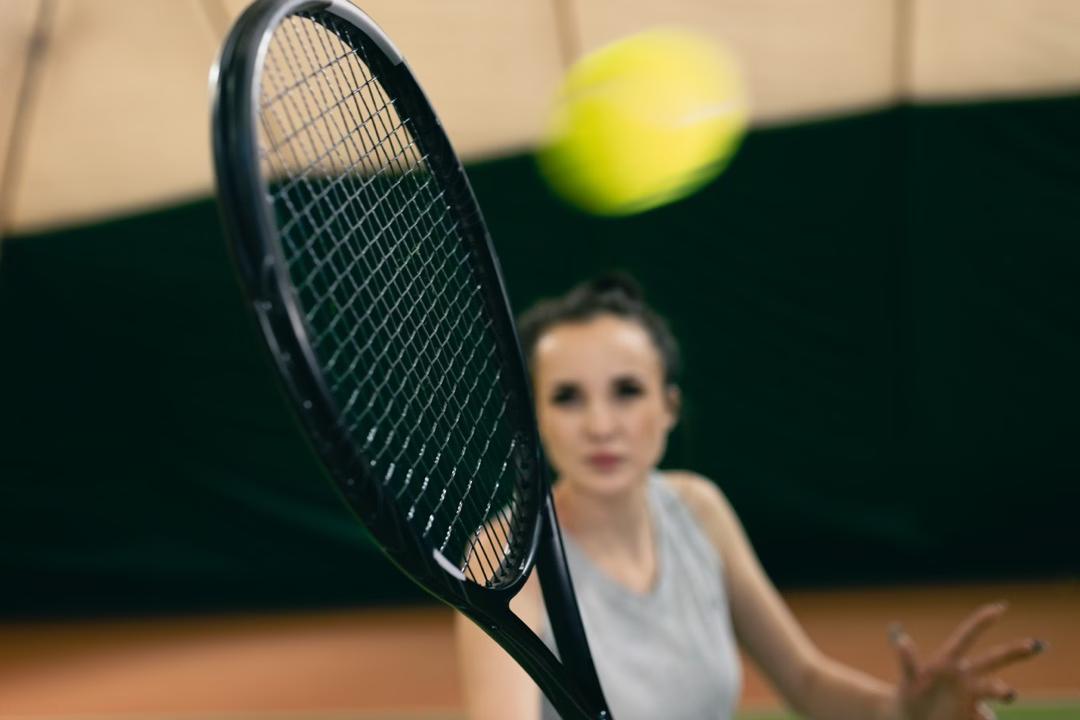Eine Frau hält ihren Tennisschläger nah an die Kamera und schlägt einen Tennisball.