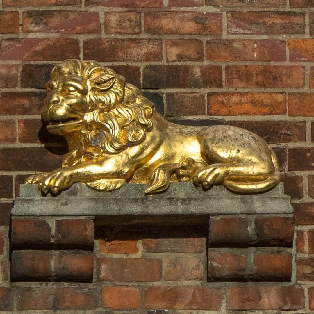 Goldene Löwenfigur auf einer Backsteinwand in Lübeck – eines der versteckten Details der St.-Marien-Tour.