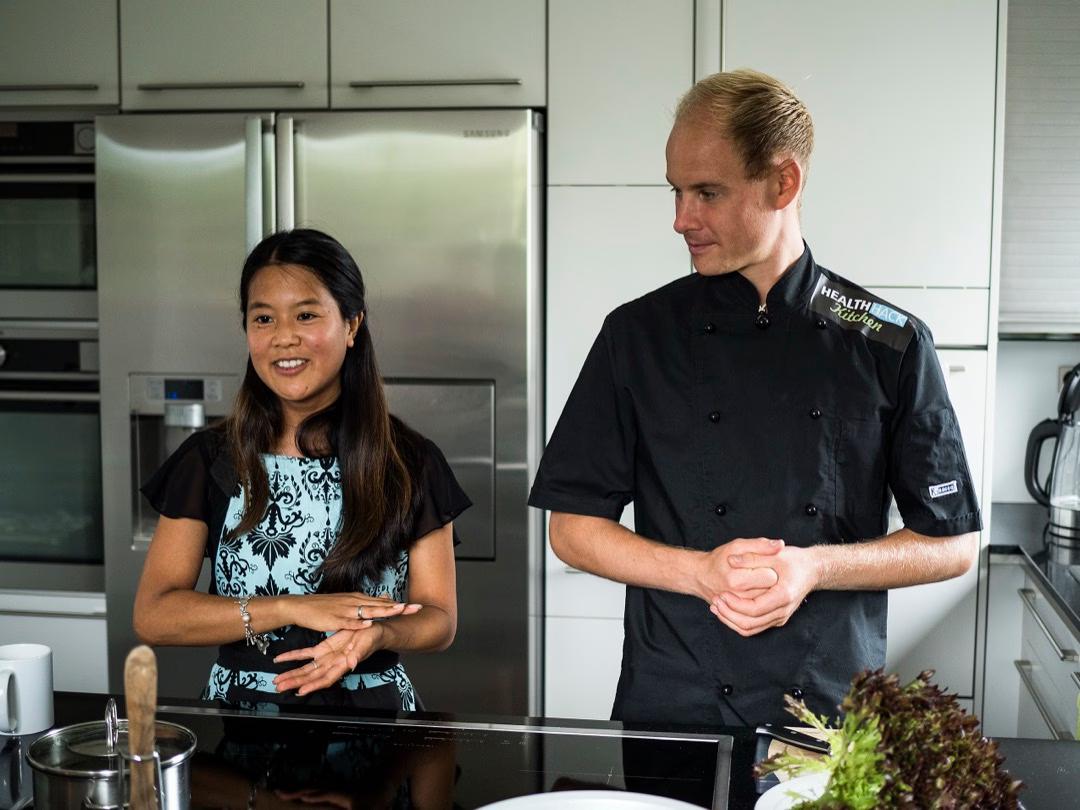 Das Küchenteam der Kochschule Health Hacks: Eine Frau und ein Mann stehen in einer Küche und leiten einen Kochkurs.