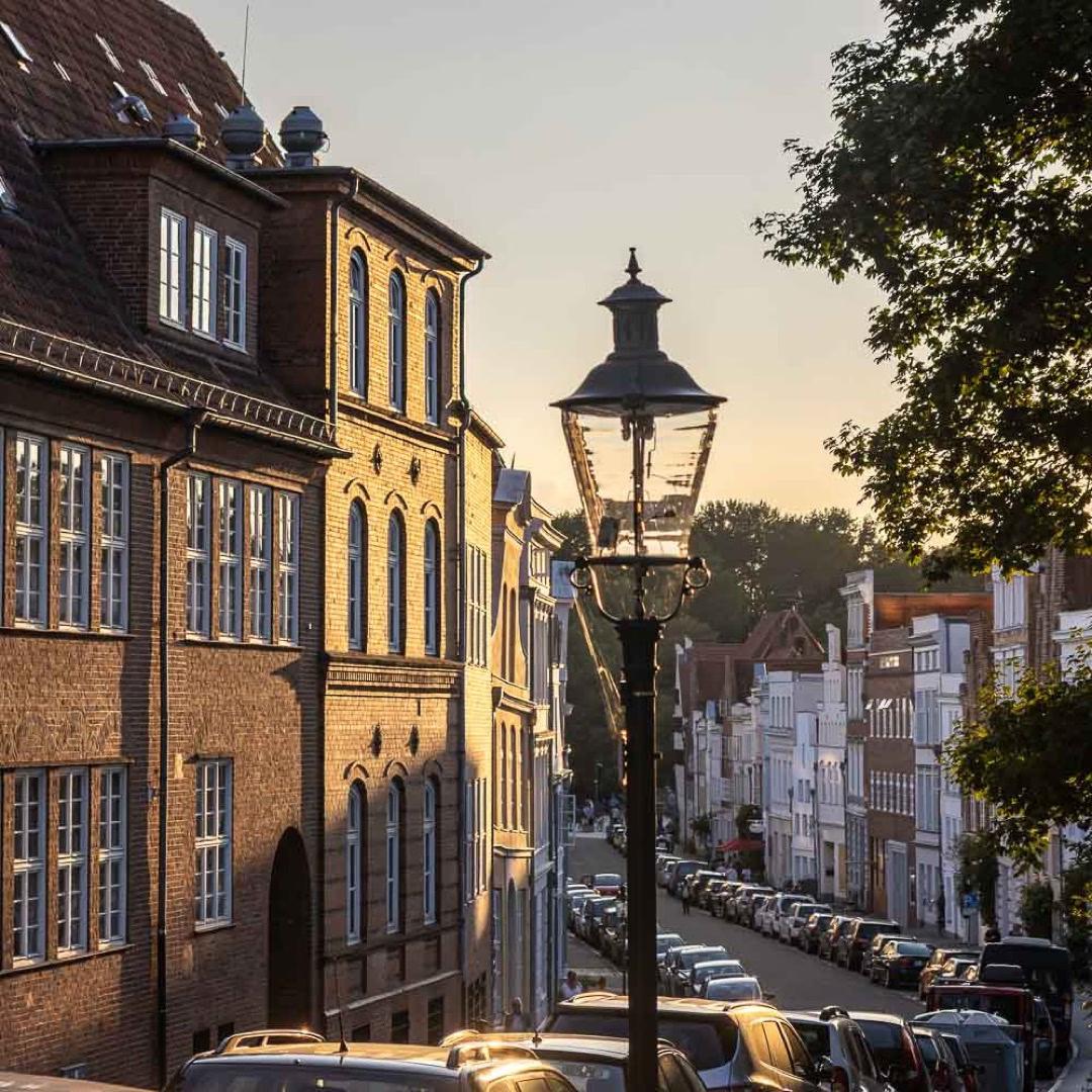 Abendstimmung in Lübeck mit historischer Straßenlaterne und Altstadthäusern im warmen Sonnenlicht.