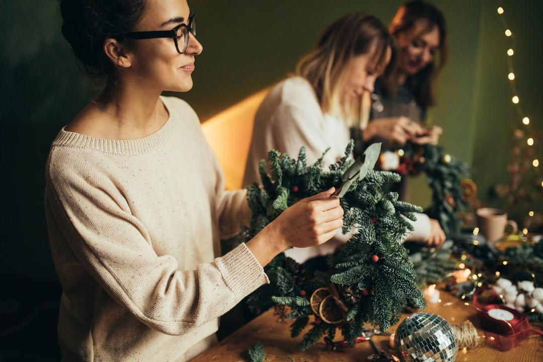 Drei Frauen stehen am Tisch und binden Adventskränze im DIY-Workshop: Adventskranz binden in Lübeck.