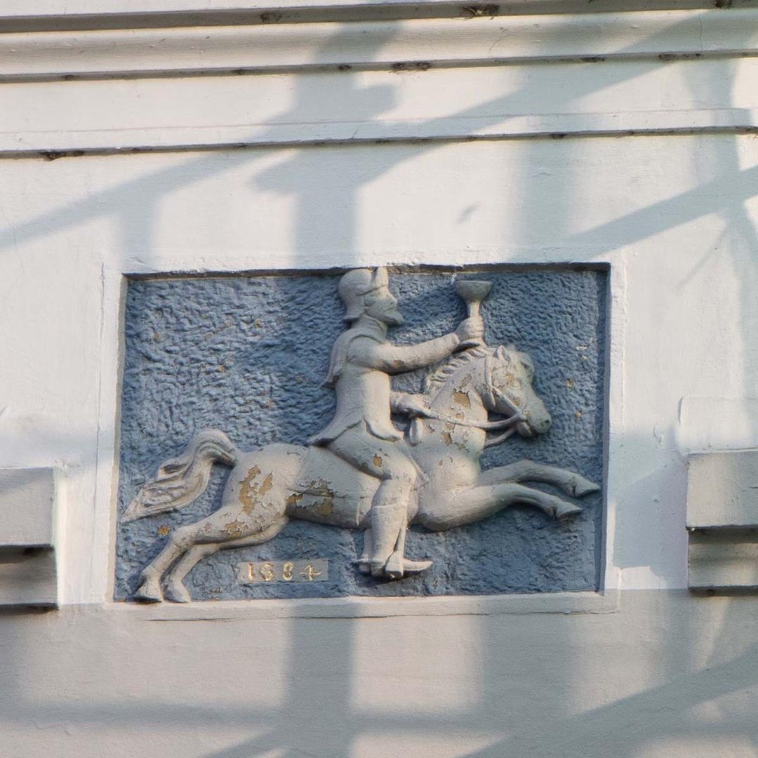 Relief eines reitenden Mannes mit Becher an einer weißen Fassade in Lübeck, datiert auf das Jahr 1884.