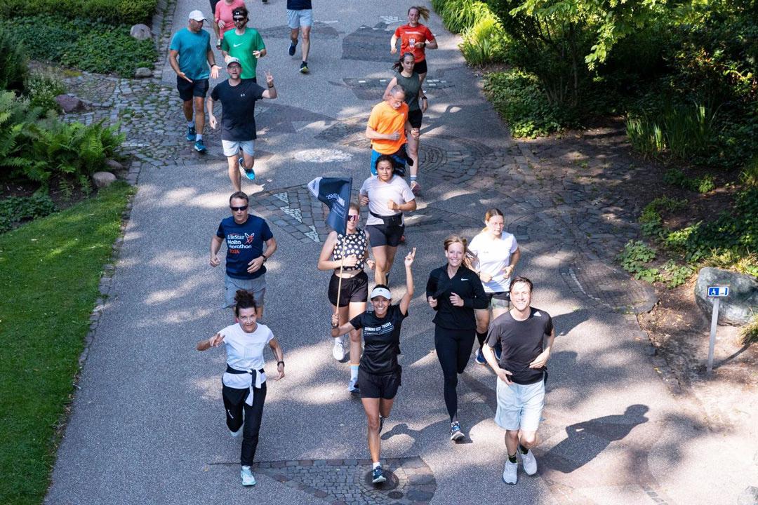 Eine fröhliche Gruppe läuft bei der Jogging-Stadtführung gemeinsam durch einen Park und winkt lachend in die Kamera.