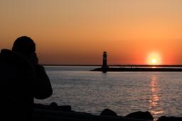 Eine Person fotografiert den Sonnenaufgang hinter der Hafenmole Warnemünde