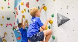 Ein Junge klettert an Griffe und Tritten an einer Boulder-Wand in der Kletterhalle Felshelden