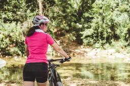 Eine Frau mit Fahrrad steht an einem kleinen Teich