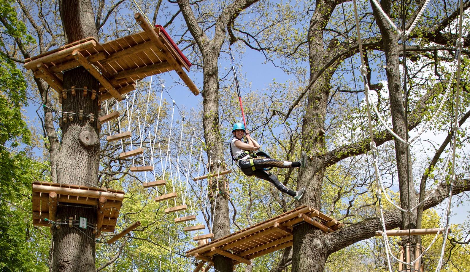 Frau schwingt sich im Klettergarten Travemünde an einer Seilrutsche von Baum zu Baum