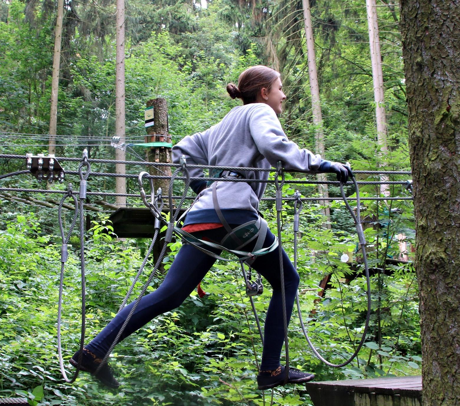 Eine Frau geht sich im Kletterwald Hohe Düne über eine Hängebrücke