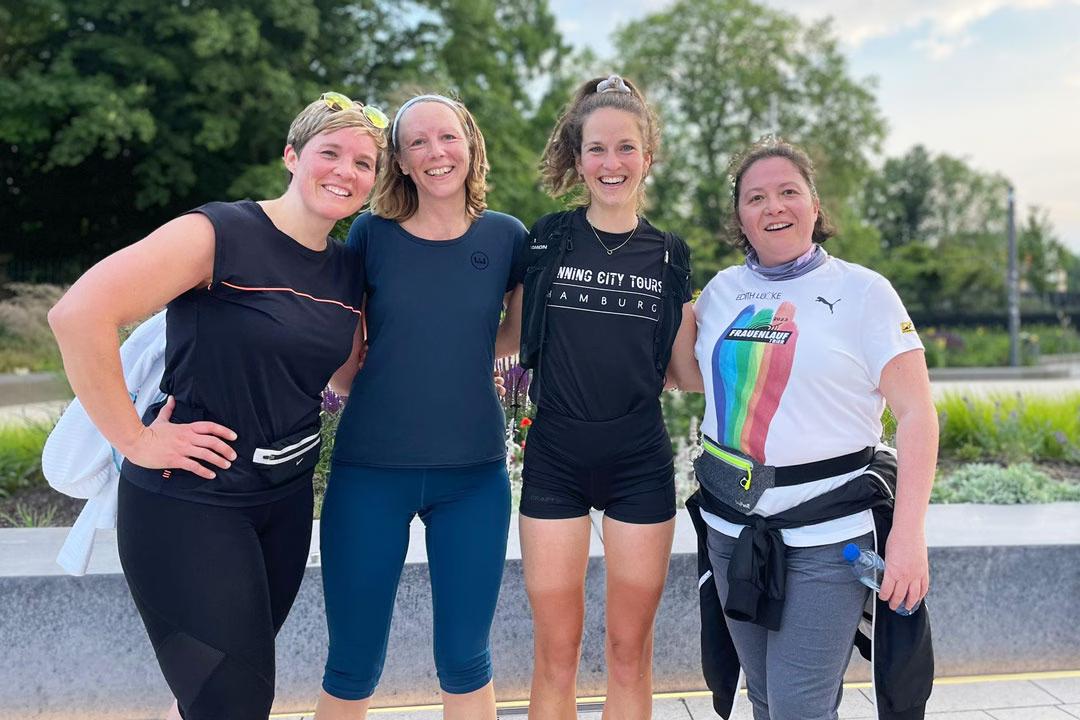 Vier Frauen in Sportkleidung, davon eine Laufführerin von Running City Tours, stehen vor einem Park und lachen.