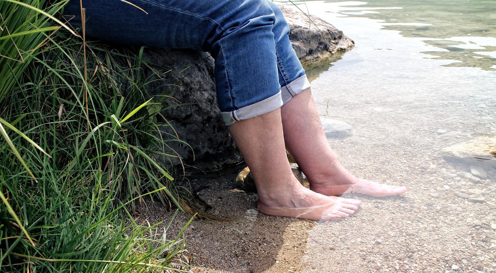 Eine Person sitzt auf einem Felsen am Fluss und hält die nackten Füße ins Wasser