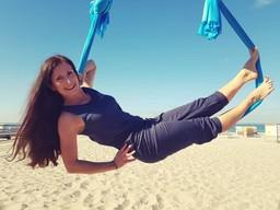 Eine Frau hängt am Strand in einem Aerial-Yoga-Tuch