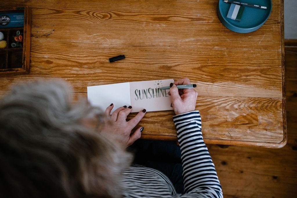 Eine Frau schreibt mit Handlettering den Schriftzug Sunshine auf eine Karte
