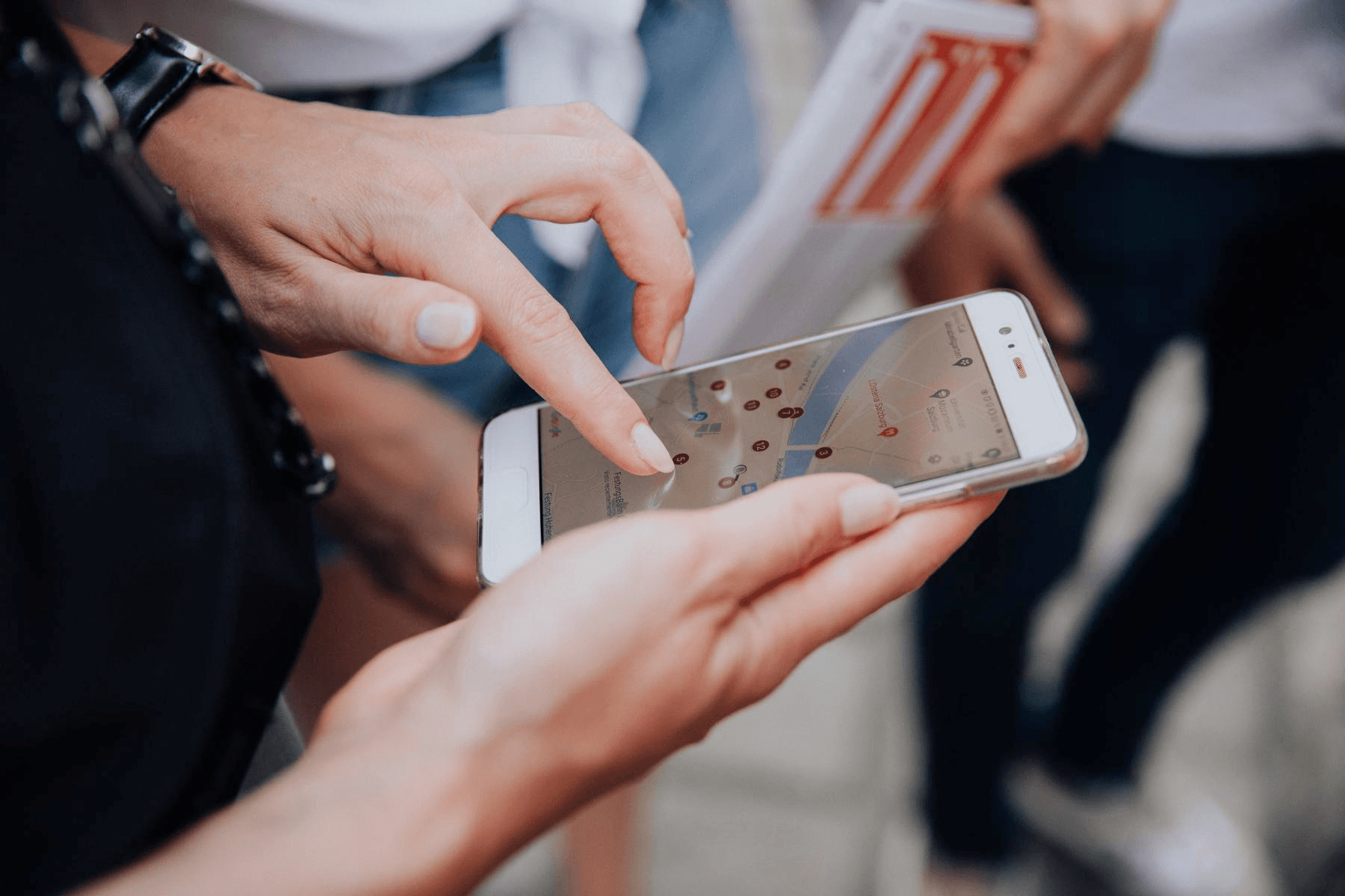 Eine Person tippt auf einem Smartphone, auf dem ein Stadtplan mit Markierungen für einen Krimi-Trail zu sehen ist