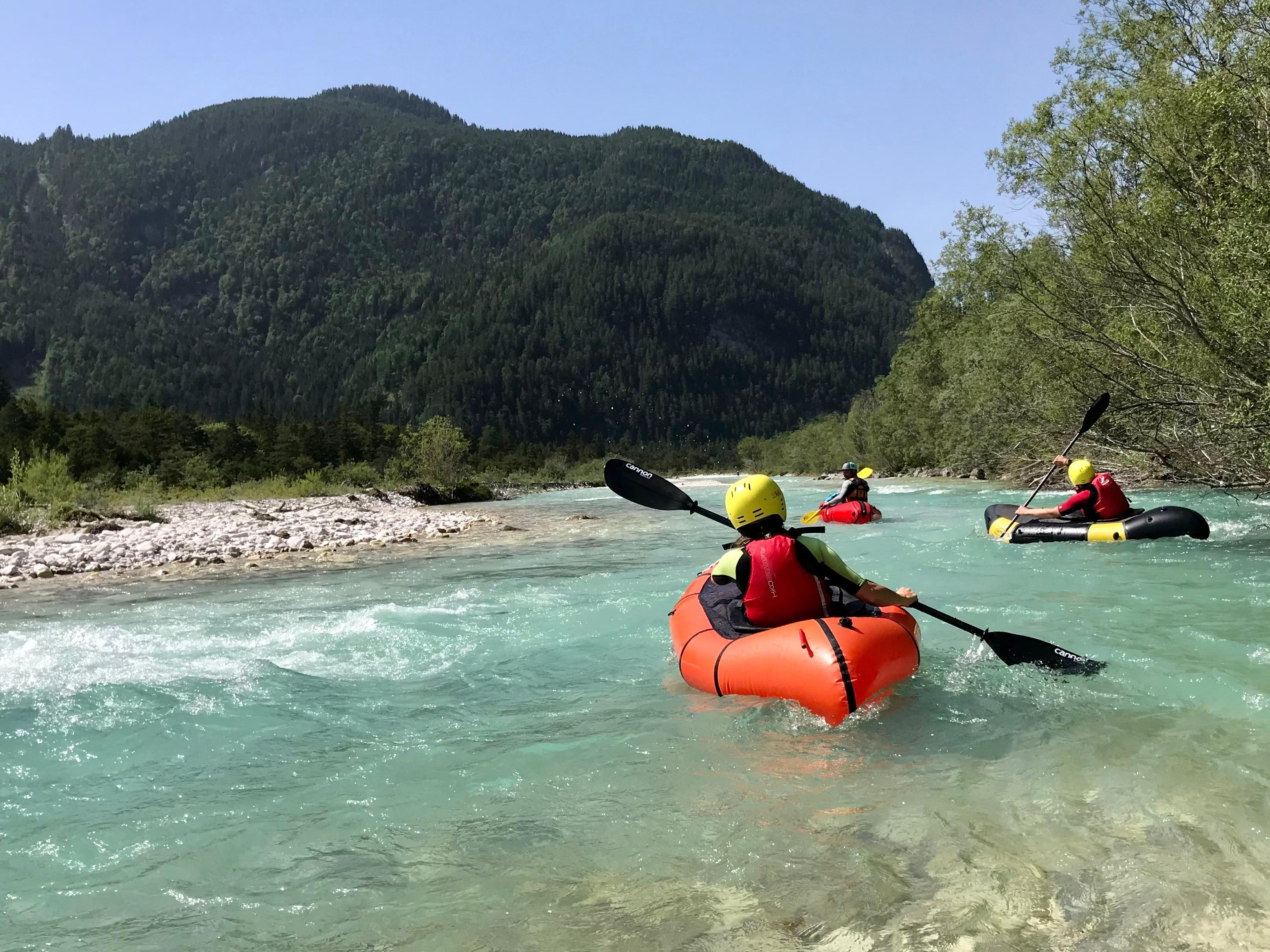 Drei Personen befahren in Packrafts einen Gebirgsfluss