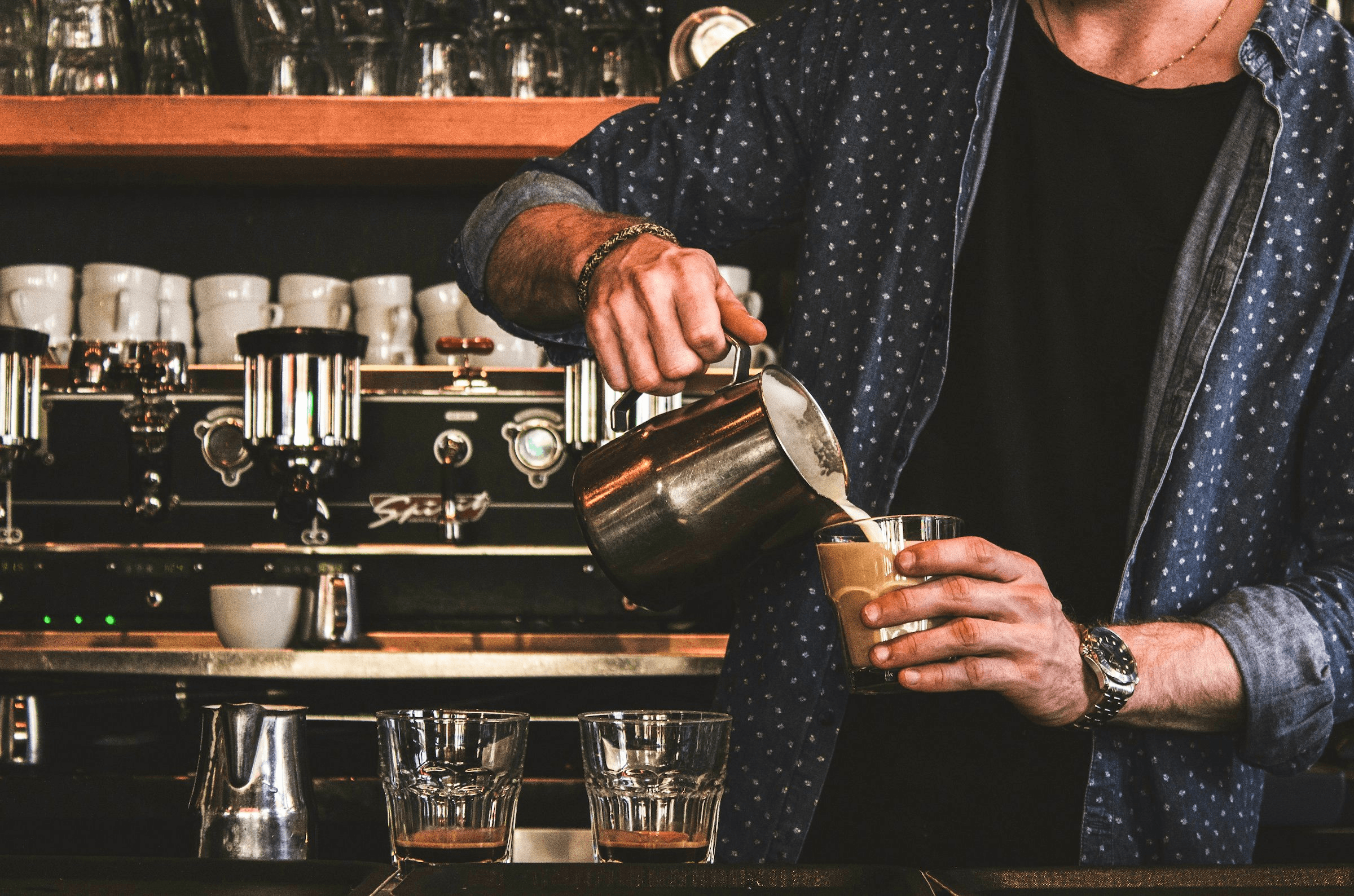 Eine Person gießt bei einem Barista-Workshop geschäumte Milch in ein Glas mit Espresso