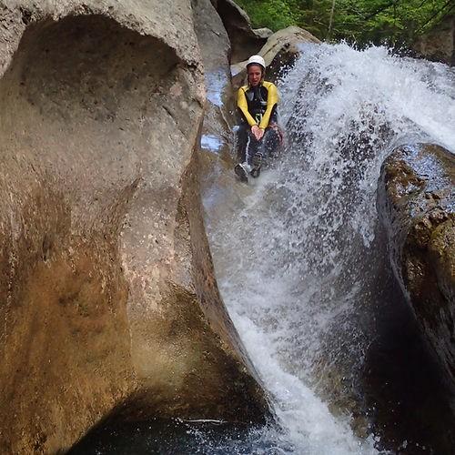 Eine Person rutscht beim Canyoning in der Starzlachklamm eine natürliche Wasserrutsche hinab