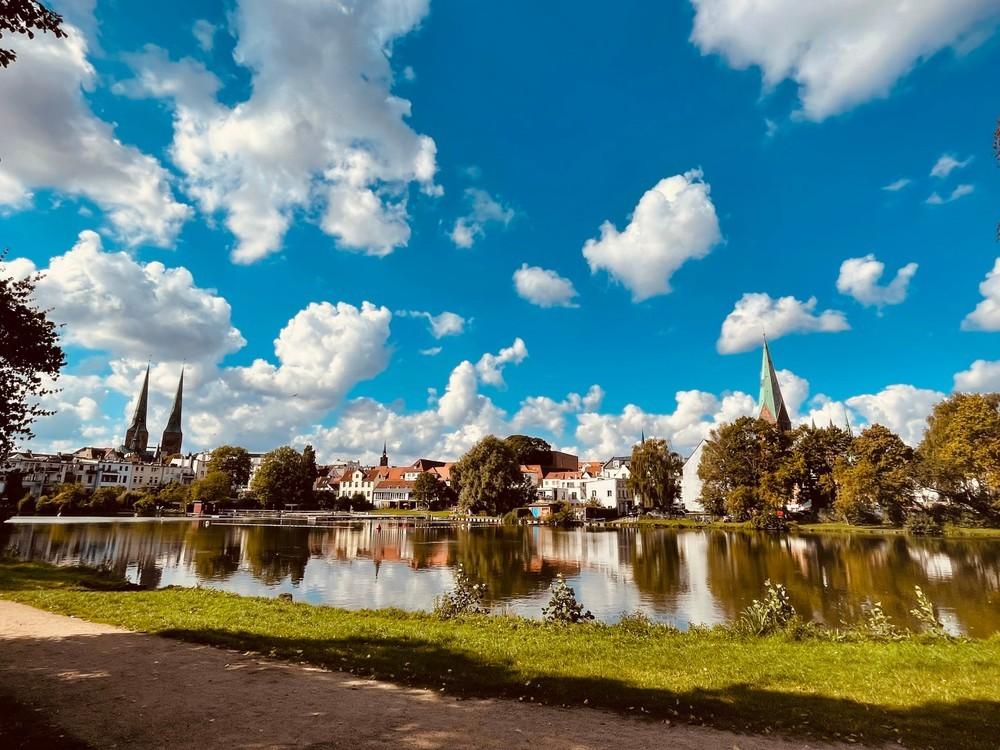 Eine Ansicht der Stadt Lübeck hinter einem von Bäumen umstandenen See