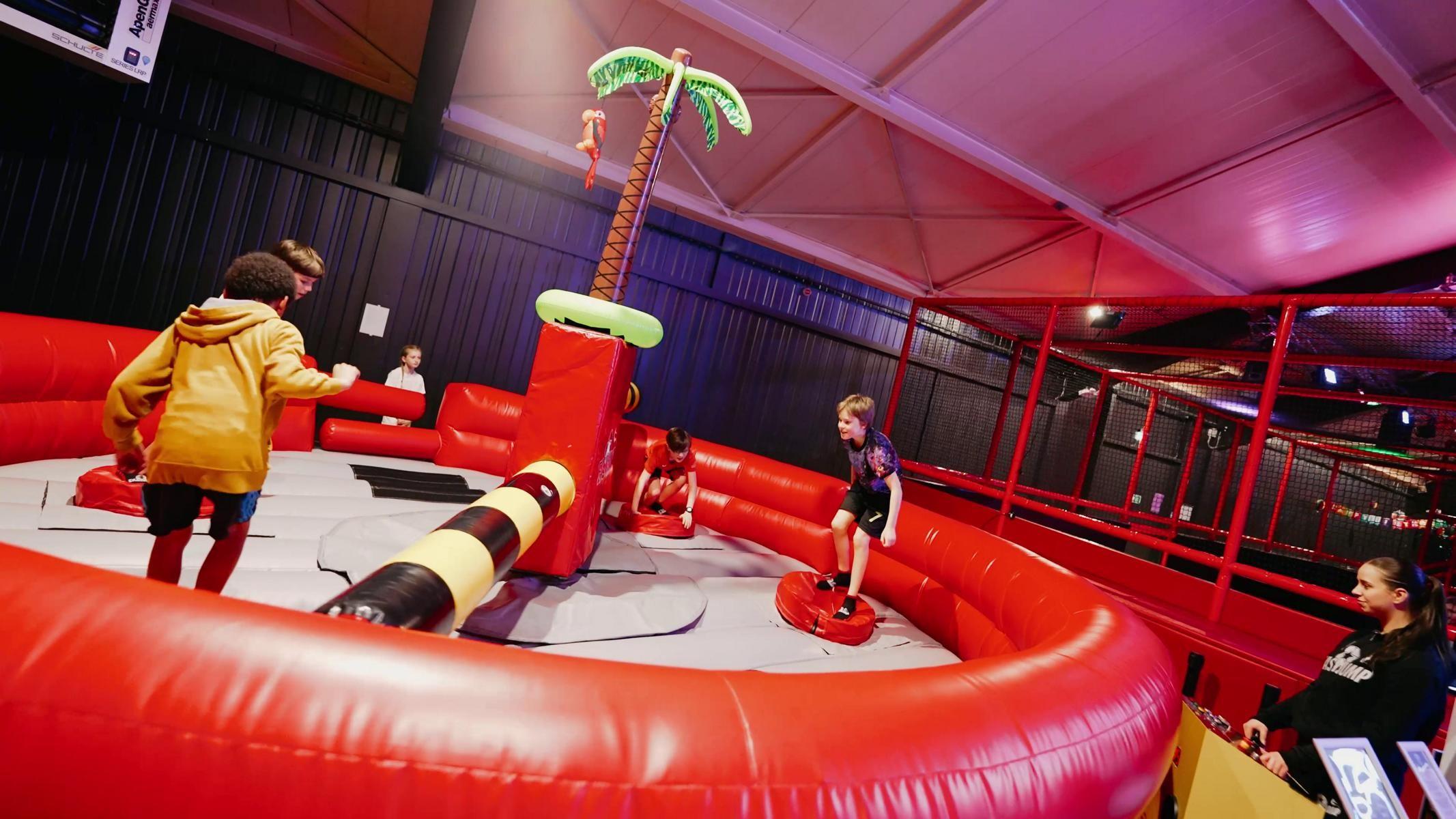 Kinder auf einem Trampolin weichen einem rotierenden Balken aus