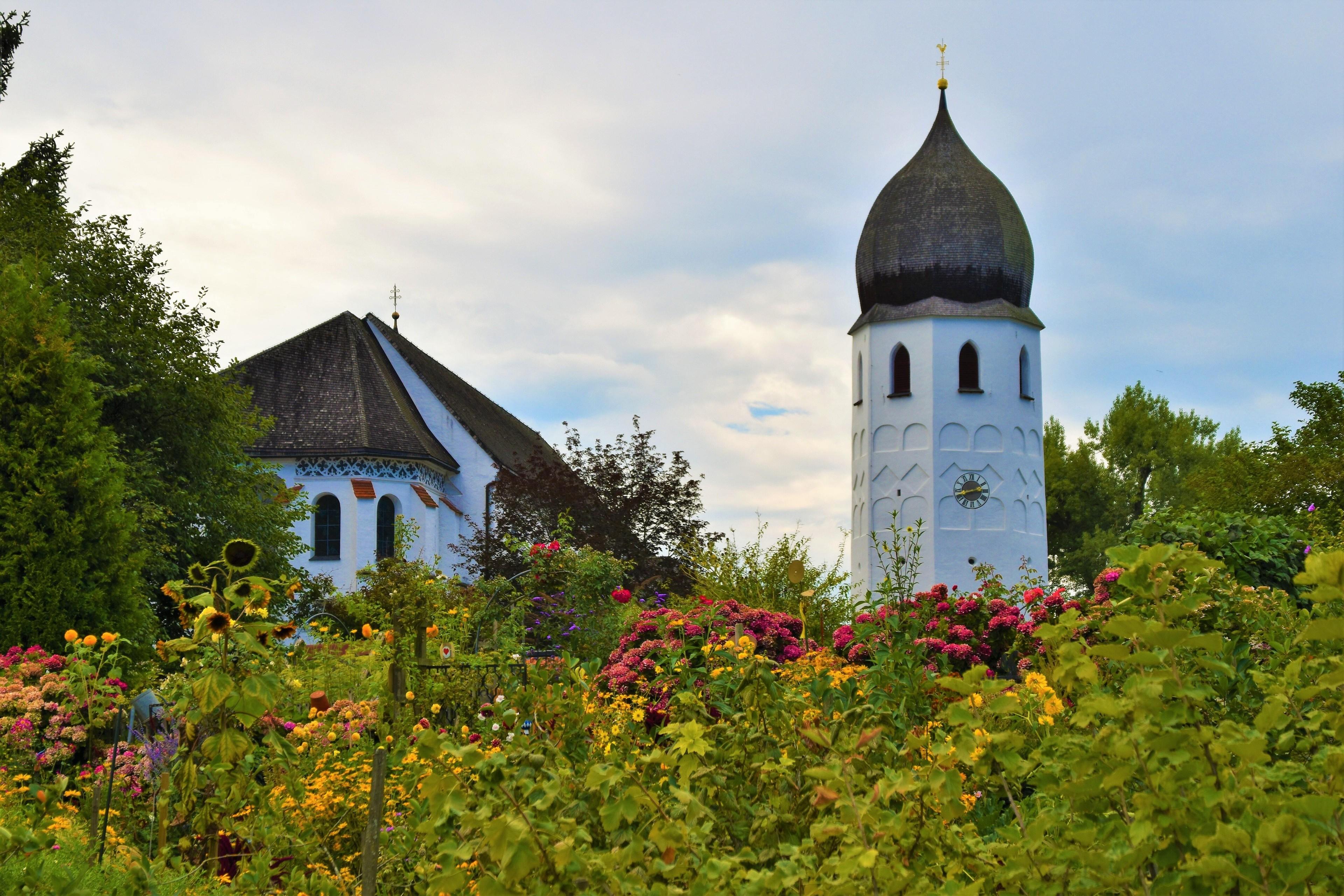 Bunte Blumen in einem Garten auf der Fraueninsel mit dem Kloster Frauenchiemsee im Hintergrund