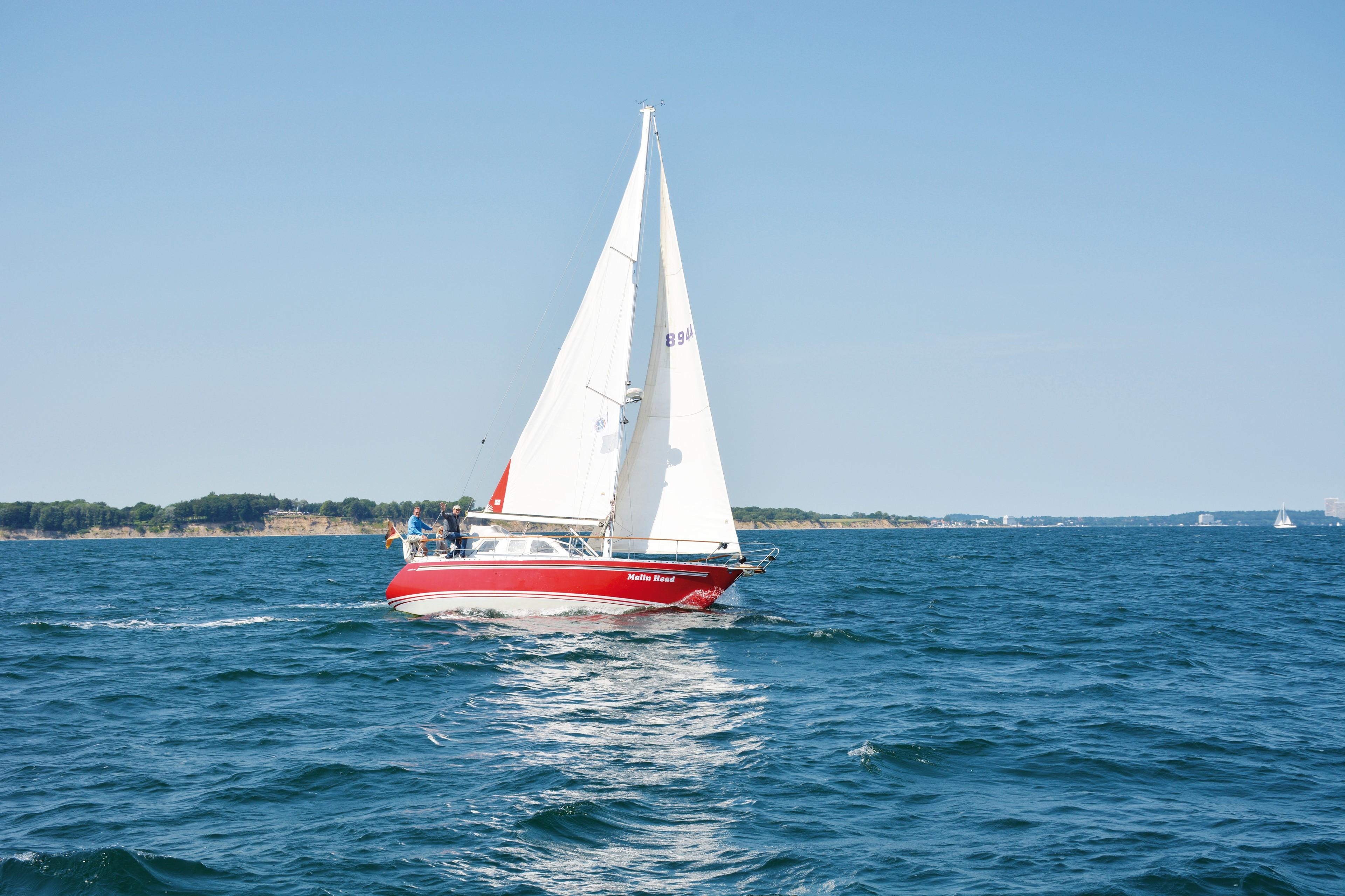 Ein Segelboot mit rotem Rumpf und weißen Segeln auf der Ostsee