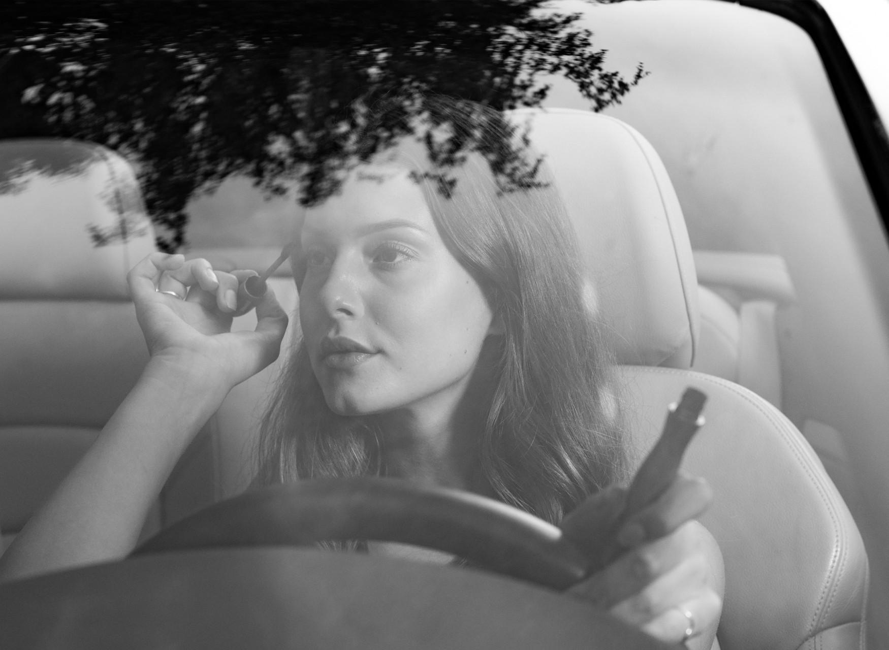 Eine Frau sitzt am Steuer eines Autos und schminkt sich mit Wimperntusche