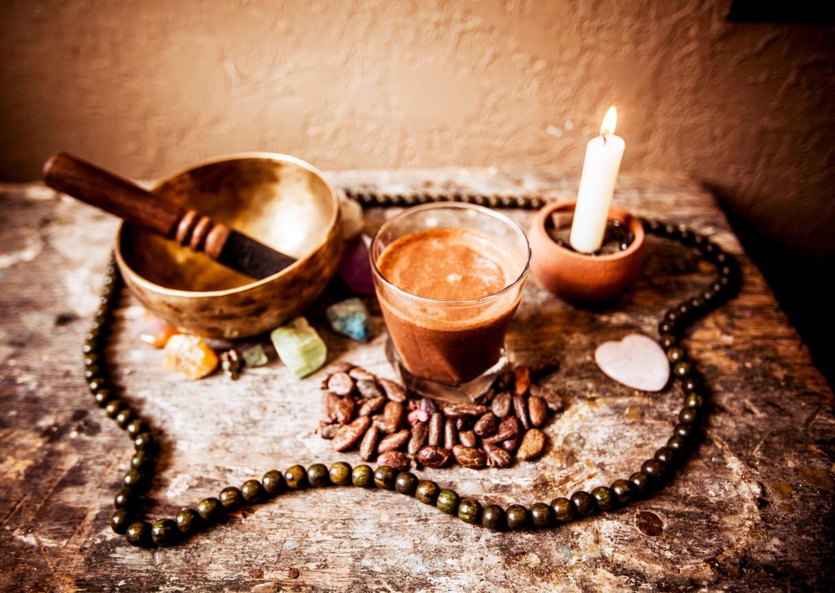 Eine Klangschale, eine Kerze und ein Glas Kakao stehen für eine Kakaozeremonie auf einem Tisch
