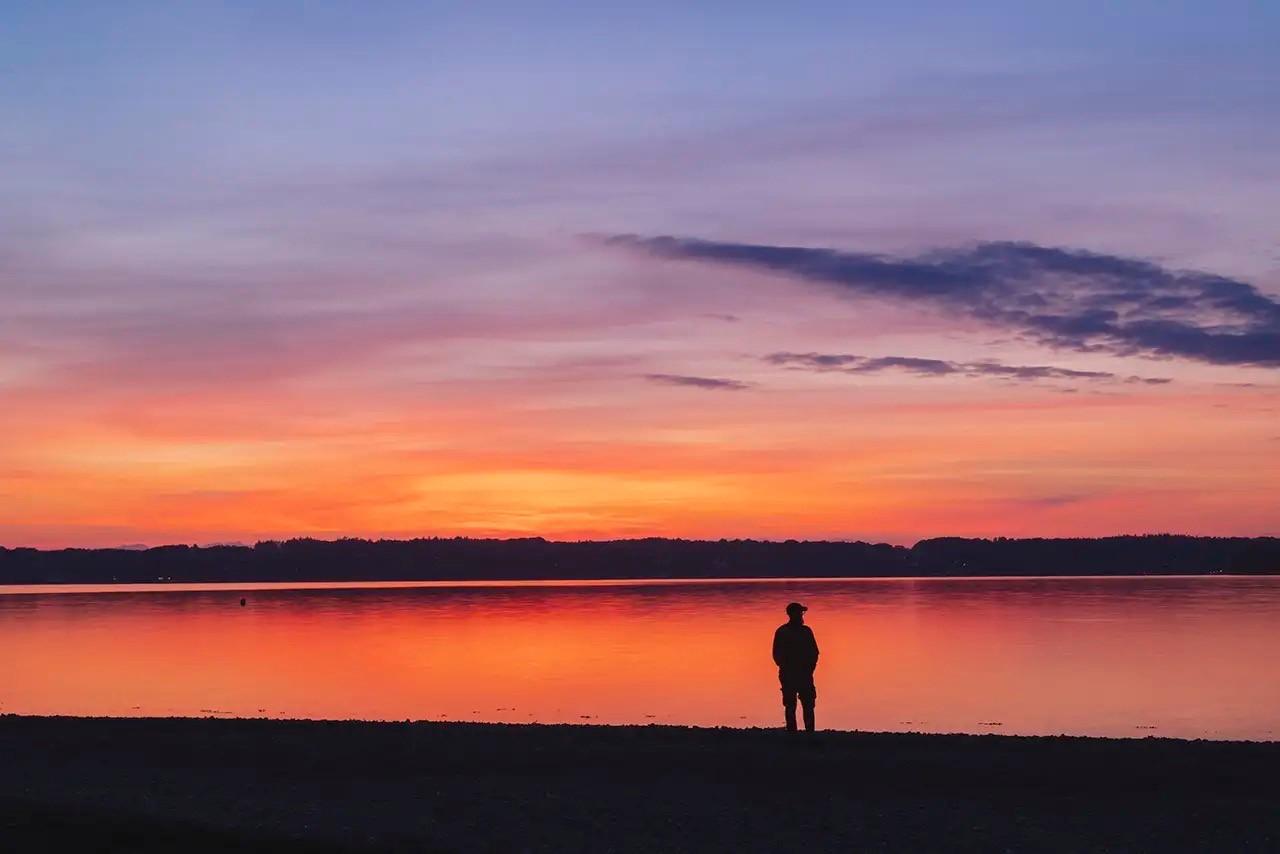 Eine Person steht bei Sonnenuntergang an einem See