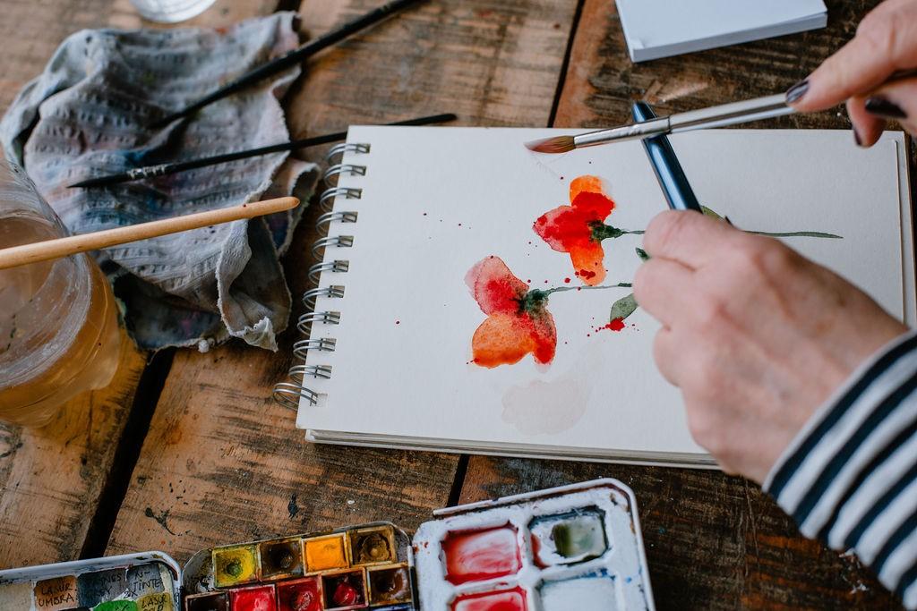 Rote Blumen in Aquarell-Technik auf einem Block Papier, Pinsel und Farben