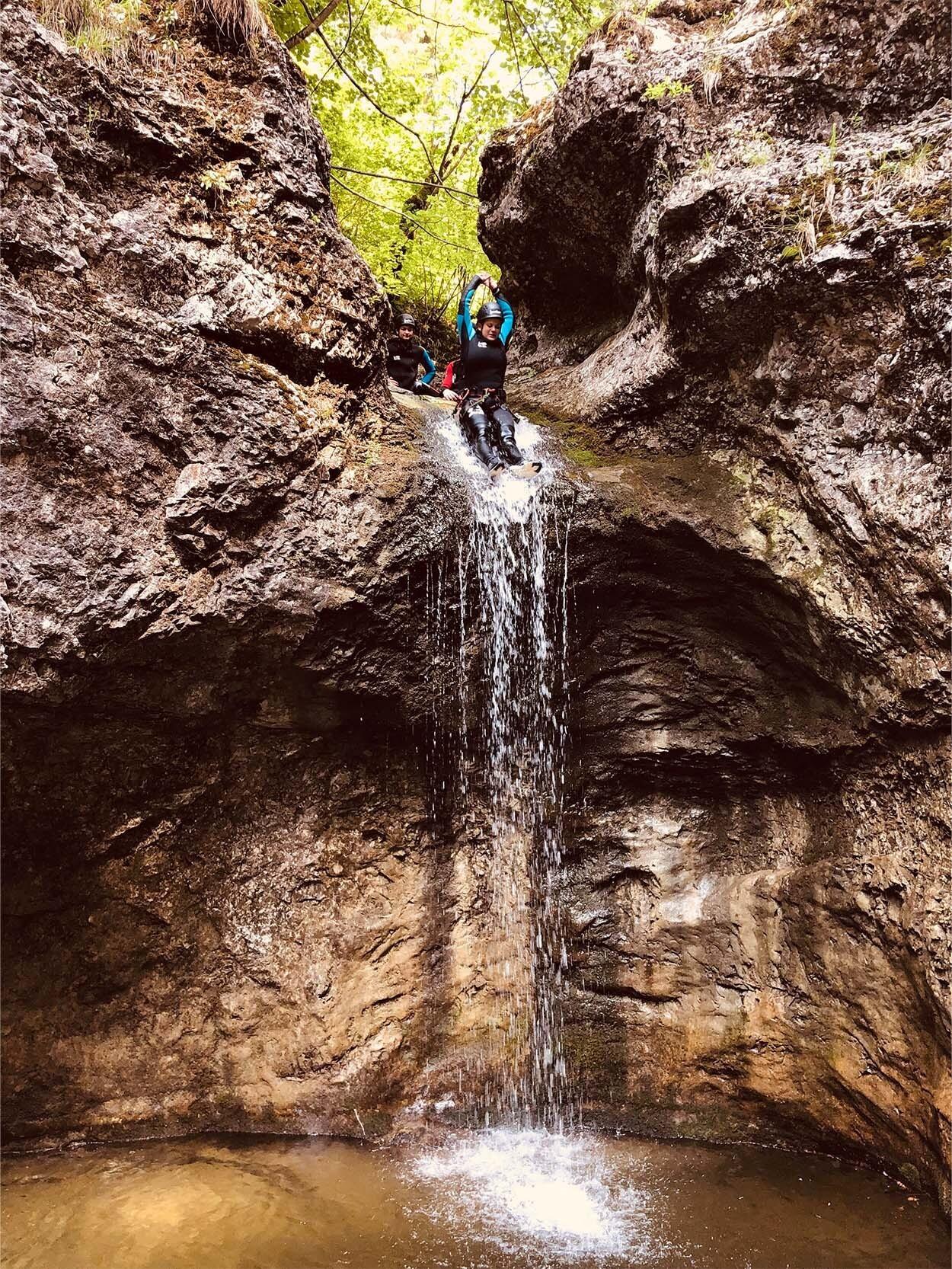 Eine Person rutscht beim Canyoning auf einer natürlichen Wasserrutsche einen Wasserfall hinab